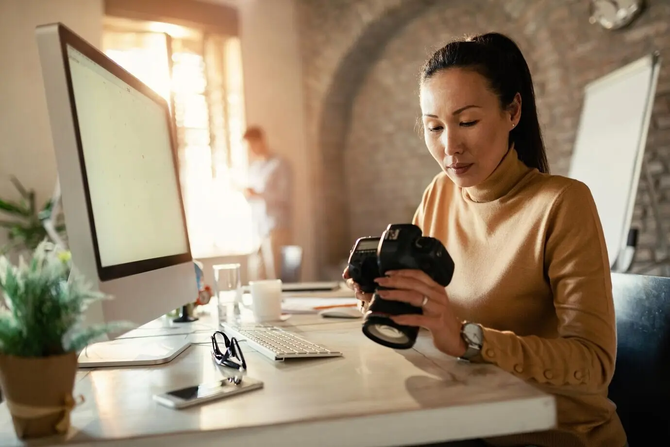An Asian photographer reviews images on a digital camera as she works in her office.